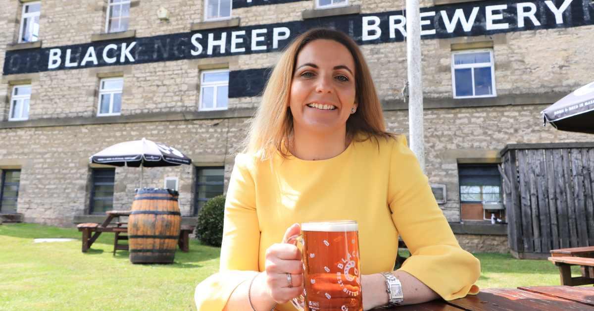 Photo of Charlene Lyons, CEO of Black Sheep Brewery, enjoying a pint outside the brewery in Masham.