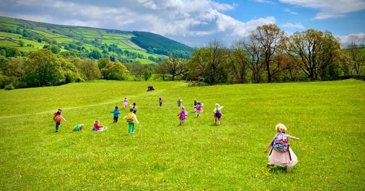 Children running across a meadow under blue skies in Nidderdale.