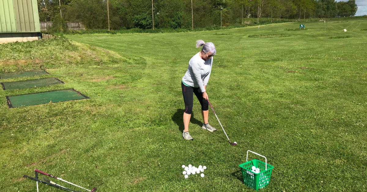Photo of female golfer lining up a shot from one of the outside bays at Ripon Golf Range, with a green basket of golf balls in the foreground.