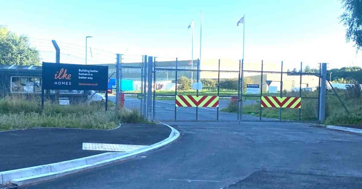 Photo of the main entrance to the Ilke Homes factory site at Flaxby, showing chain-link fencing and barbed wire.