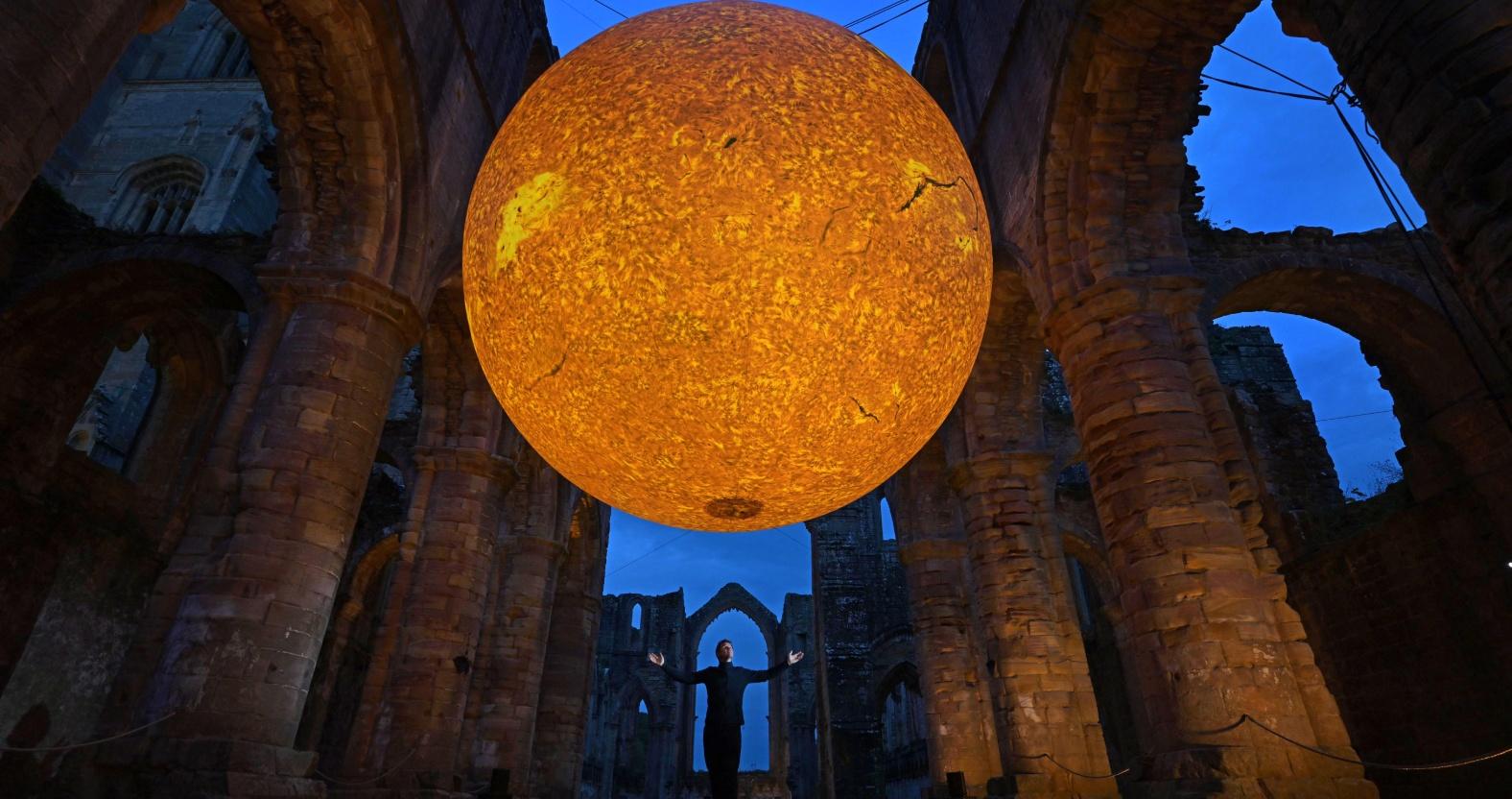 artist-luke-jerram-stands-underneath-helios-suspended-in-the-nave-of-fountains-abbey-credit-anthony-chappell-ross-1