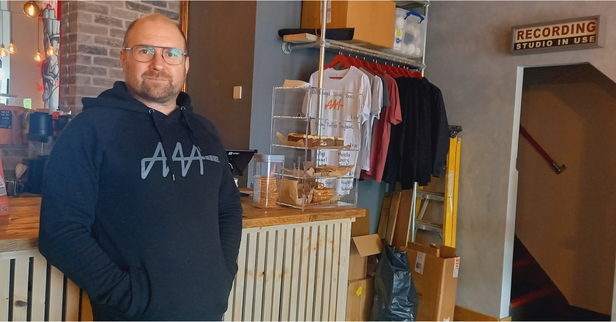 Photo of sound engineer Dave Swallow, who has opened AAA (pronounced 'triple A'), a vinyl coffee house and bar on Cold Bath Road in Harrogate. This picture shows Dave leaning against the bar, with a lit-up sign above the door to the stairway that says 'Recording Studio In Use'.
